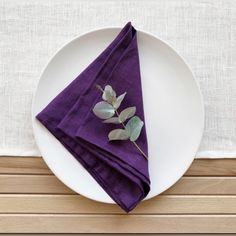 a white plate topped with a purple napkin next to a leafy green plant on top of a wooden table