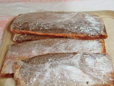 three pieces of fish sitting on top of a wooden cutting board with plastic wrap around them