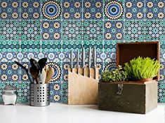 an assortment of kitchen utensils in a wooden box on a counter with blue and green tiles