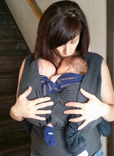 a woman is holding a baby in her arms while wearing a grey vest and blue socks