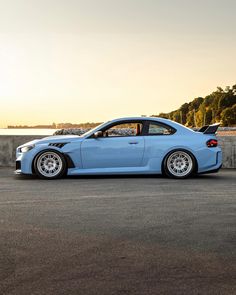 the blue car is parked on the side of the road by the water at sunset