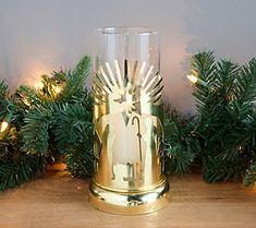 a gold candle holder sitting on top of a wooden table next to evergreen branches and lights