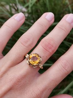 a woman's hand with a yellow ring on top of her finger and grass in the background