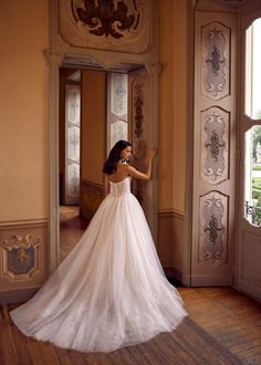 a woman in a white wedding dress is standing by an open door and looking out the window