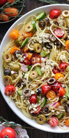 a white bowl filled with pasta and vegetables on top of a table next to tomatoes