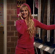 a woman in a red hoodie talking on a cell phone while standing next to a brick wall