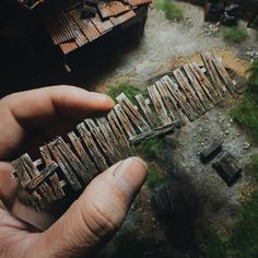 a hand holding up some type of wooden object in front of an old building and grass