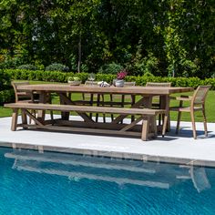 an outdoor table and chairs next to a swimming pool with trees in the back ground