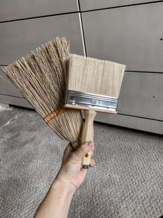 a hand holding a paint brush on top of a gray rug in front of a wall