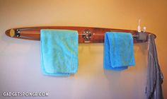 two towels hanging on a wall with a surfboard in the background and toothbrushes next to them