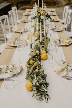 a long table is set with lemons, greenery and white candlesticks