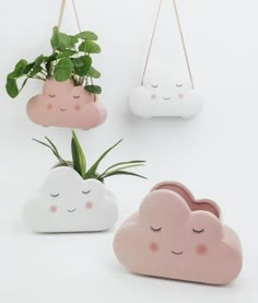 three planters with plants in them hanging from hooks on the wall, one is shaped like a cloud and the other has eyes closed