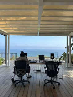 a man sitting at a desk on top of a wooden deck next to the ocean