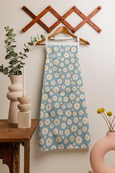 a blue and white flowered dress hanging on a wall next to a vase with flowers