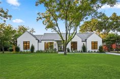 a white house sitting in the middle of a lush green field next to a tree