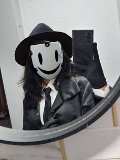 a person in a suit and hat taking a selfie with a cell phone while wearing a smiley face mask