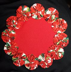 a red and white flowered circle with green leaves on black fabric in the center