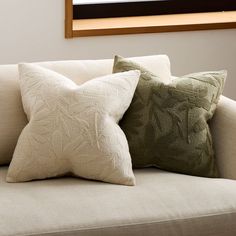 two pillows are sitting on a couch in front of a framed painting and window above it