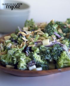 a plate full of broccoli and other food on a table with a bowl in the background