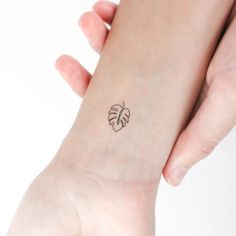 two hands holding each other with a small tattoo on the wrist that has a leaf