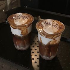 two glasses of iced coffee sitting on top of a black table with white and brown toppings