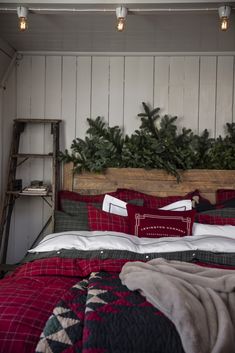 a bed with red and black comforter next to a wooden headboard filled with pine branches