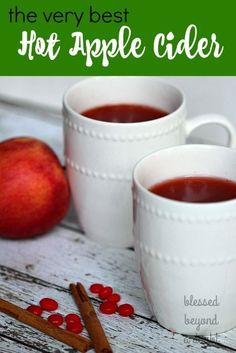 two white mugs filled with hot apple cider next to cinnamon sticks and an apple