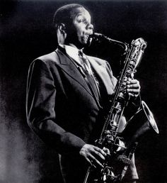 a black and white photo of a man playing a saxophone in front of a microphone