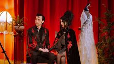 a man and woman sitting in front of a red curtain