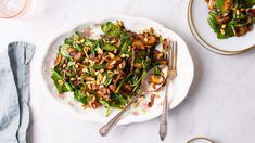 a white plate topped with salad next to two plates filled with greens and nuts on top of a table