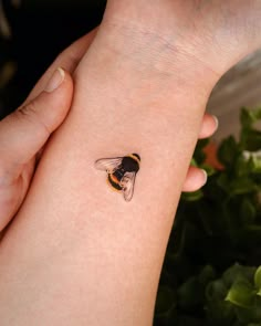 a woman's arm with a small tattoo of a bee on the left wrist