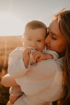 a woman holding a baby in her arms and kissing it's face with the sun shining