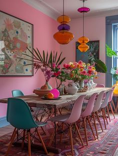 a dining room with pink walls and wooden table surrounded by colorful chairs, plants and vases