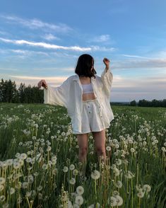 a woman standing in the middle of a field with dandelions