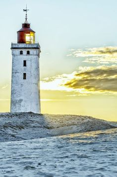 a light house sitting on top of a sandy beach next to the ocean at sunset