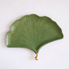 a large green leaf shaped dish hanging from the side on a white wall with gold accents