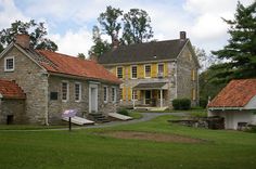 an old stone house with yellow shutters on the windows and red roof, surrounded by lush green grass