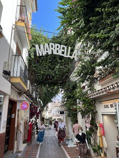 people walking down an alley way with trees growing on the sides and buildings in the background