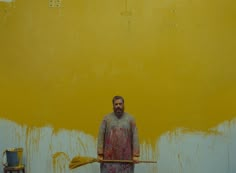 a man with a broom standing in front of a yellow wall