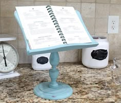 a recipe book on a stand in the middle of a kitchen counter with two clocks behind it