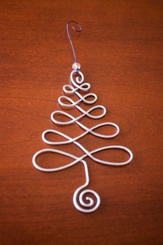 a wire christmas tree ornament hanging on a wooden table with a metal hook