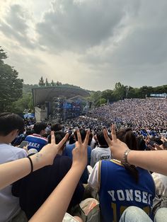 a crowd of people sitting in front of a stage with their hands up to the sky