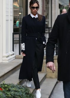 a man and woman walking down the street in front of a building wearing black coats