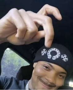 a man wearing a black hat and holding his hand up to the camera while sitting in a car