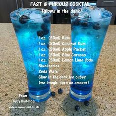 two glasses filled with blue liquid and ice on top of a counter next to each other