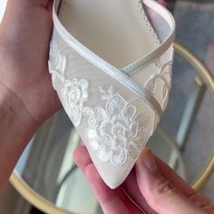 a person holding up a white shoe with flowers on the bottom and lace around it