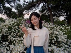 a woman standing in front of flowers making the peace sign