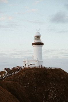 a lighthouse on top of a hill with people walking up the stairs to it in the distance