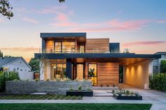 a large modern home with lots of windows and landscaping on the front lawn at dusk