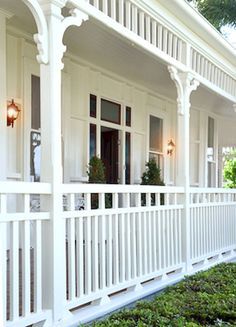 the front porch of a house with white railings and green bushes on either side